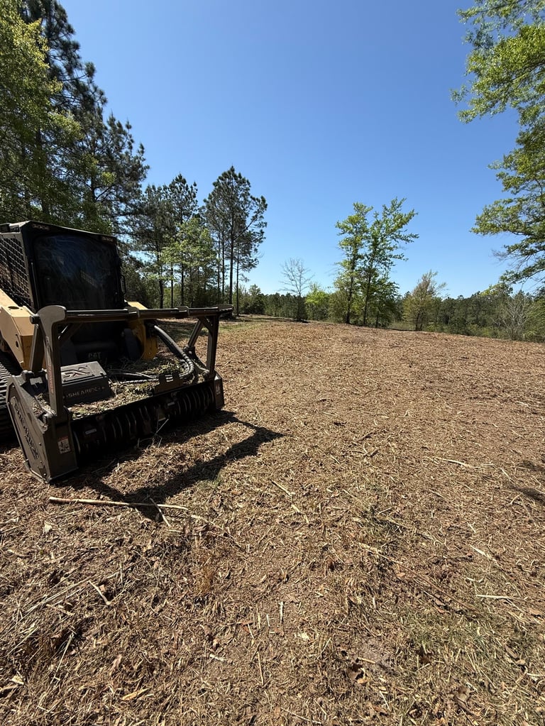Old farm equipment with black bin on a dirt field under clear sky with tree line in background